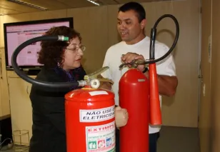O bombeiro militar Alisson Rodrigo de Oliveira orienta Roseli de Fátima dos Santos a usar corretamente o extintor de incêndio
